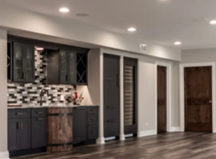 Finished basement with dark cabinetry, tile backsplash and wood-look floor