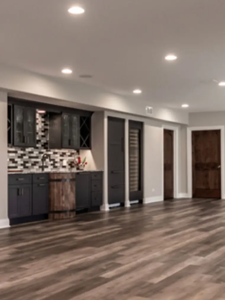 Finished basement with dark cabinetry, tile backsplash and wood-look floor