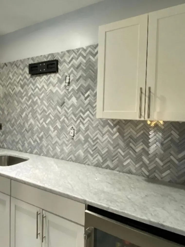 Herringbone marble backsplash under white cabinets