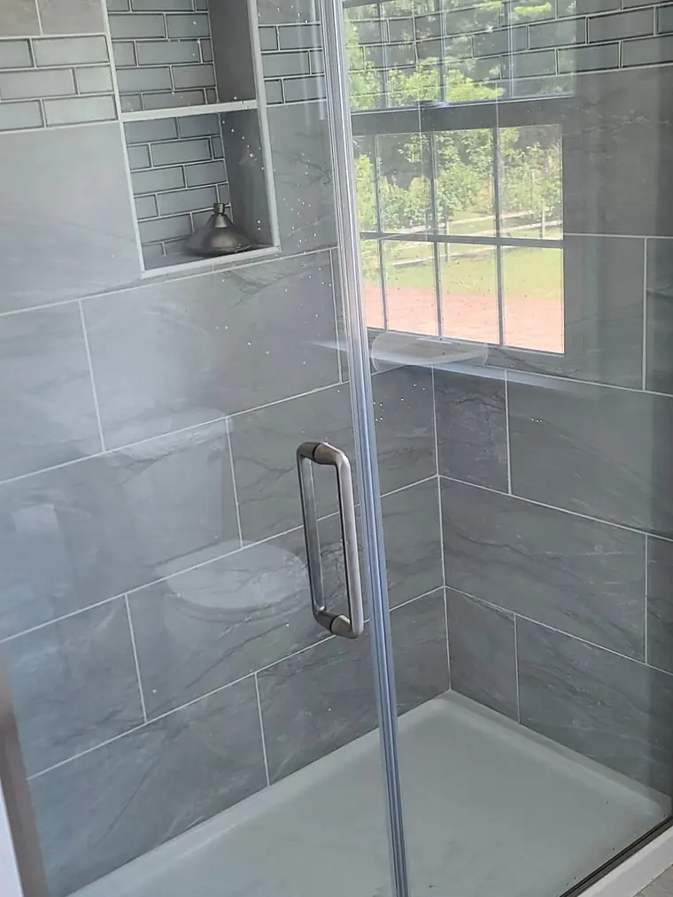 Gray tiled shower with a window and glass door