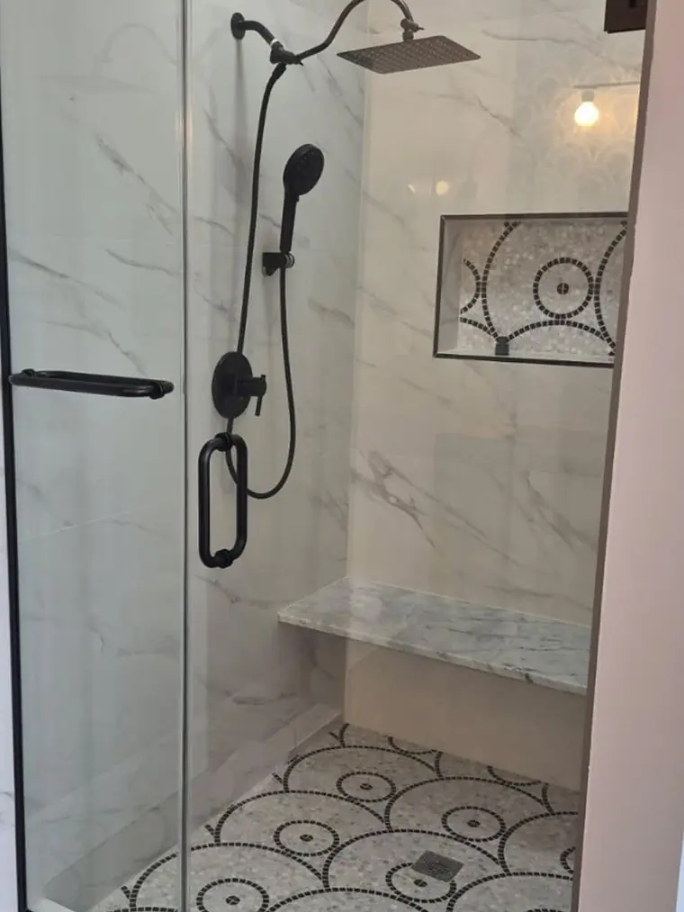 Marble shower with black fixtures and a mosaic accent